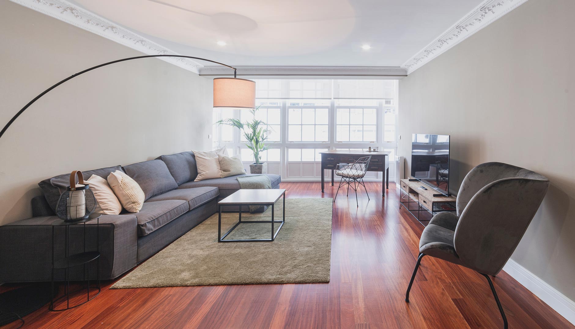 Salón amplio y luminoso con sofá en L, escritorio y TV en apartamento de alquiler en A Coruña